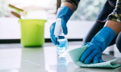 Husband housekeeping and cleaning concept, Happy young man in blue rubber gloves wiping dust using a spray and a duster while cleaning on floor at home.